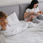 mom on bed breastfeeding and daughter pretending with her doll