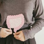 woman wearing brown holds a drawing cutout of intestines over her stomach