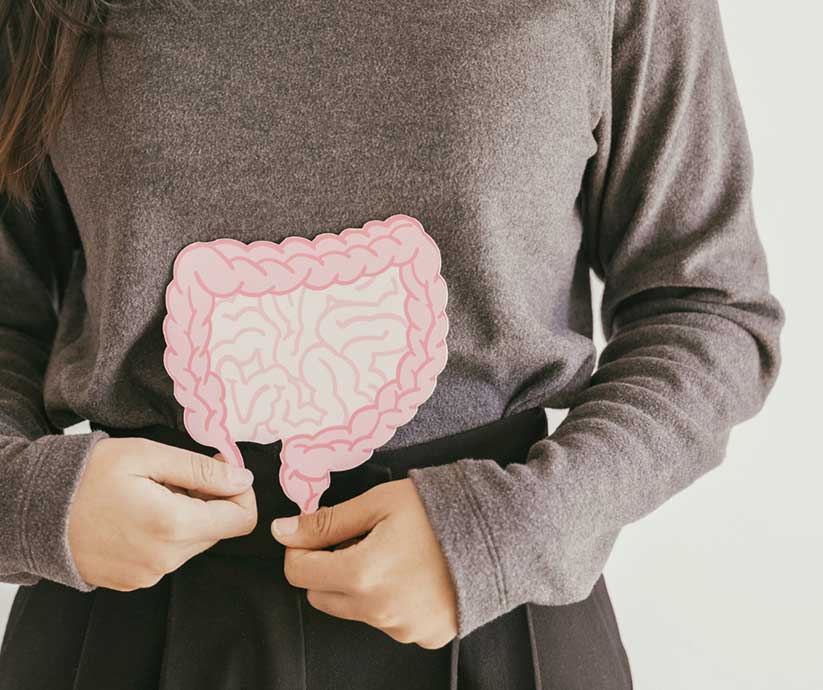 woman wearing brown holds a drawing cutout of intestines over her stomach